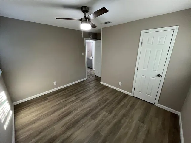 an empty room with wooden floor fan and windows