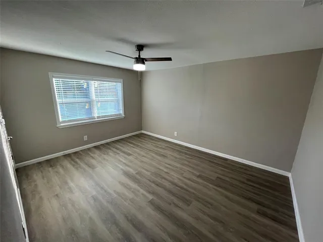 an empty room with wooden floor fan and windows