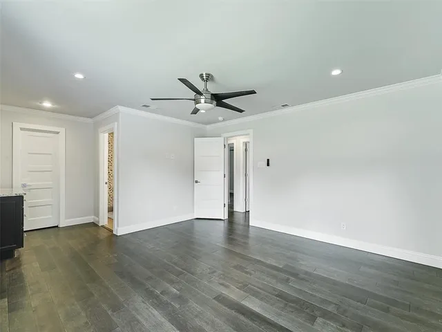 a view of an empty room with wooden floor and a ceiling fan
