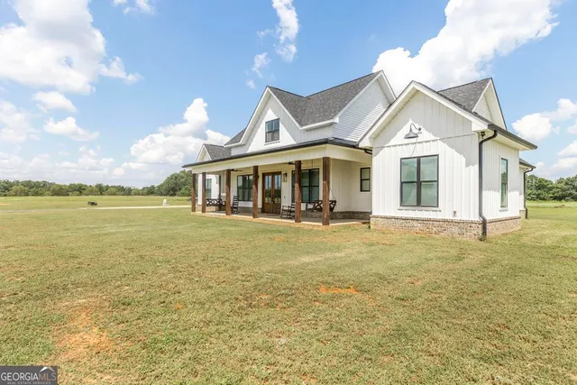 a view of a white house next to a yard with big trees