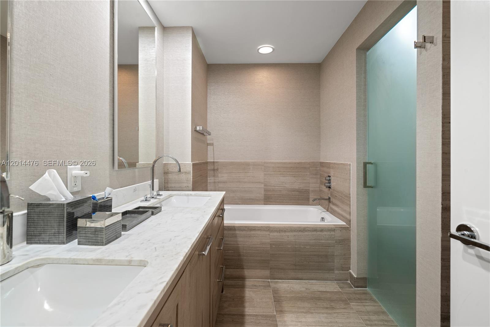 360 Ocean Drive, Unit 1106S Key Biscayne, FL 33149 - Photo 27 of 67 Primary Bathroom with Tub and Shower – This spacious bath offers a soaking tub, frosted glass shower enclosure, and extended vanity space. Warm tilework and textured wall finishes add depth to the modern design.