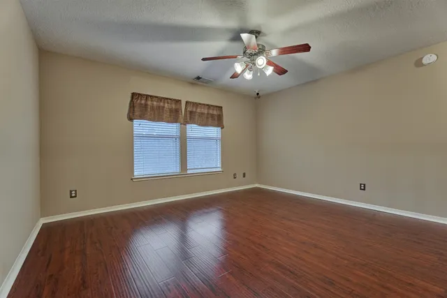 an empty room with wooden floor chandelier fan and windows