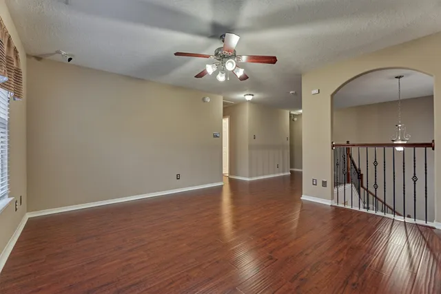 a view of an empty room with wooden floor and a ceiling fan