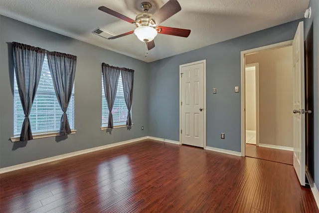 an empty room with wooden floor fan and windows