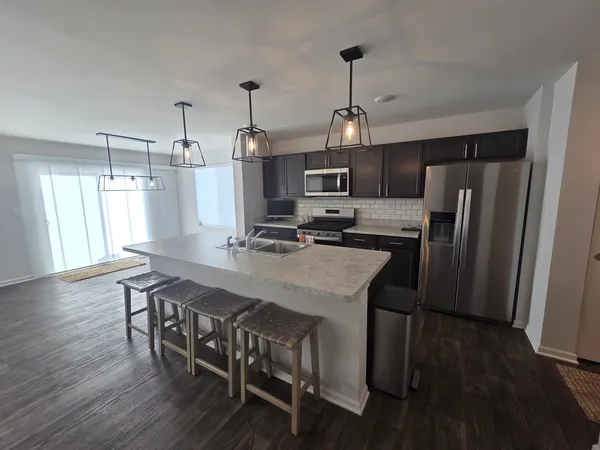 a kitchen with stainless steel appliances granite countertop a dining table chairs refrigerator and microwave