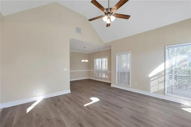 an empty room with wooden floor fan and windows