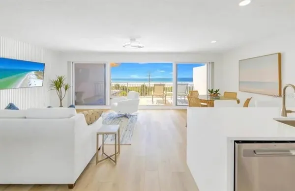 a living room with stainless steel appliances furniture a flat screen tv and a table
