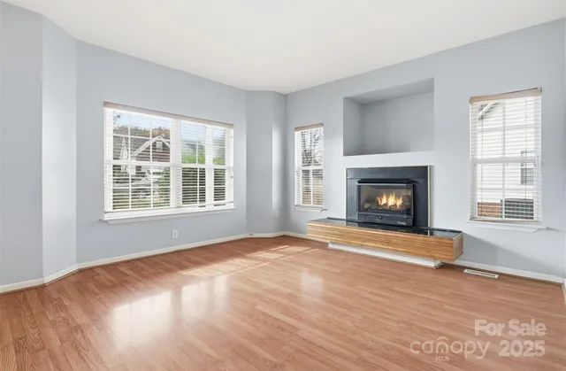 a view of an empty room with wooden floor fireplace and a window