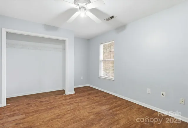 an empty room with wooden floor fan and windows