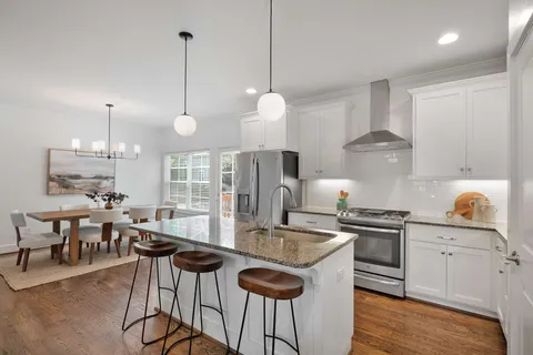 a kitchen with stainless steel appliances granite countertop a stove a sink a refrigerator a dining table chairs and white cabinets