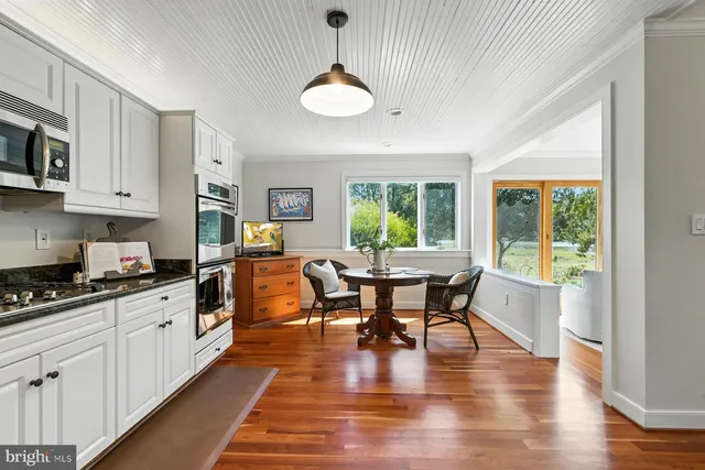 a kitchen with stainless steel appliances granite countertop a stove top oven a sink a dining table and chairs with wooden floor