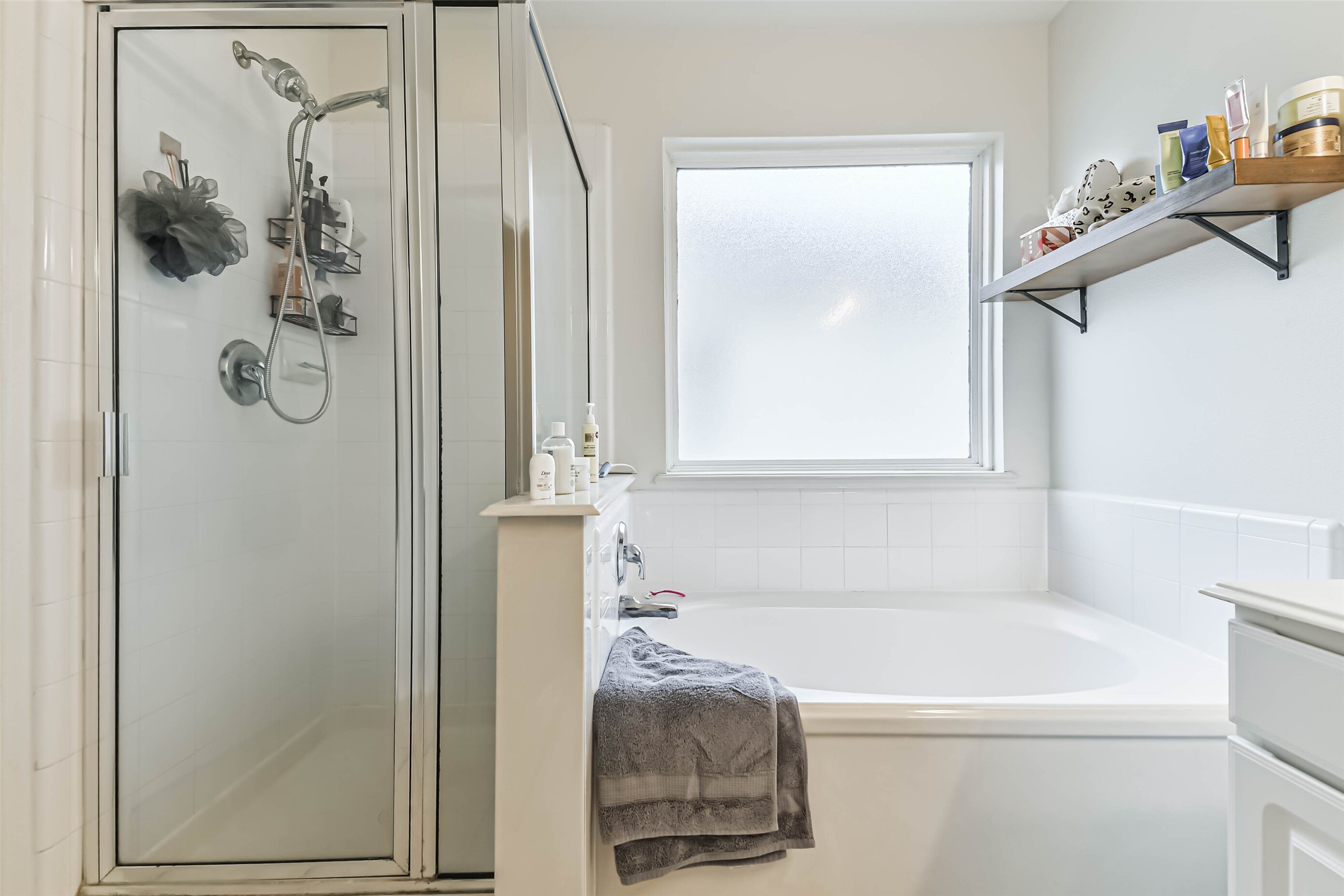 22538 Goss Spring Court Spring, TX 77373 - Photo 26 of 36 This bathroom features a spacious white bathtub next to a frosted window, a glass-enclosed shower, and sleek shelving for storage. The neutral tones and natural light create a clean and inviting space.