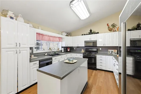 a kitchen with stainless steel appliances a stove top oven a sink a refrigerator white cabinets and wooden floor