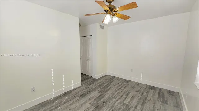 an empty room with wooden floor fan and windows