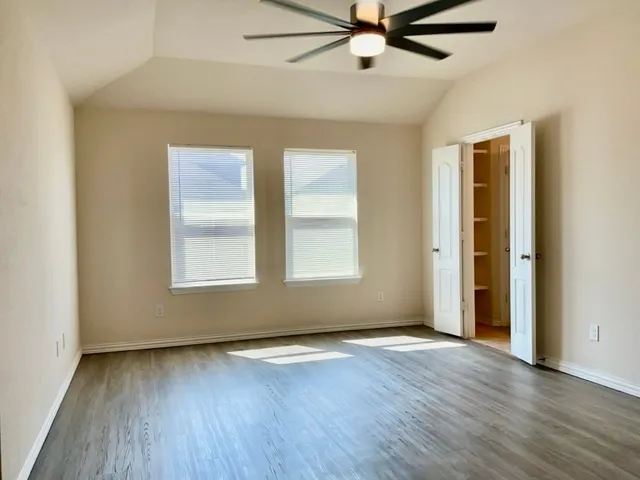 an empty room with wooden floor fan and windows