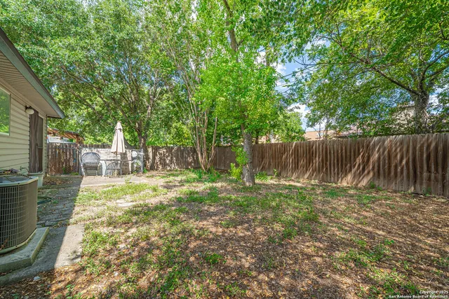 a backyard of a house with large trees and wooden fence