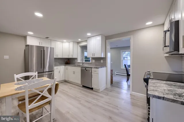 a kitchen with stainless steel appliances kitchen island granite countertop a refrigerator a stove a sink dishwasher and white cabinets with wooden floor