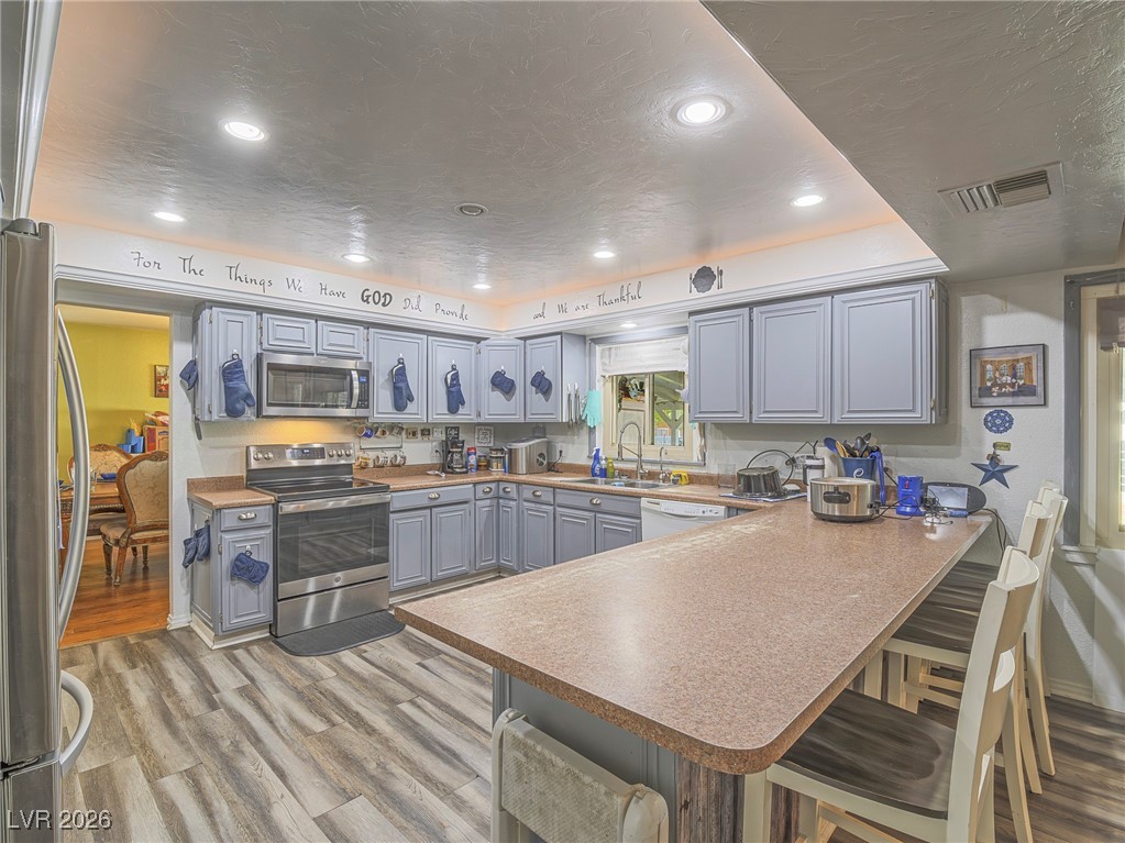846 Fairview Drive Henderson, NV 89015 - Photo 15 of 39 Kitchen featuring gray cabinets, appliances with stainless steel finishes, recessed lighting, light wood-type flooring, and a kitchen bar