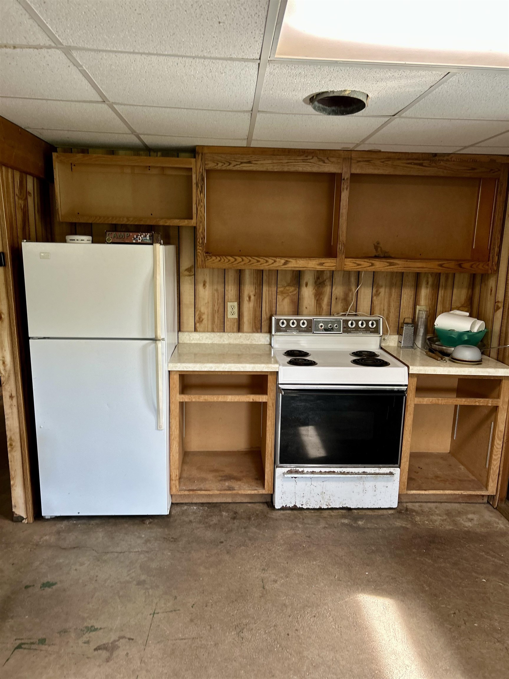 4184 Bergstrom Road Two Harbors, MN 55616 - Photo 9 of 20 Kitchen featuring a drop ceiling, white appliances, brown cabinets, concrete flooring, and wood walls