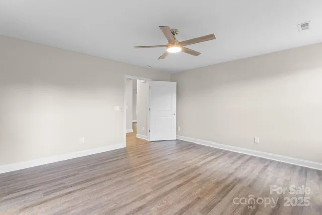 a view of an empty room with wooden floor and a ceiling fan