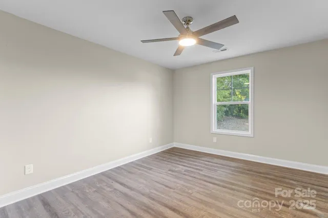 an empty room with wooden floor ceiling fan and windows