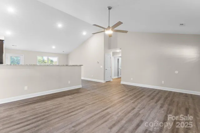 a view of an empty room with wooden floor and a ceiling fan