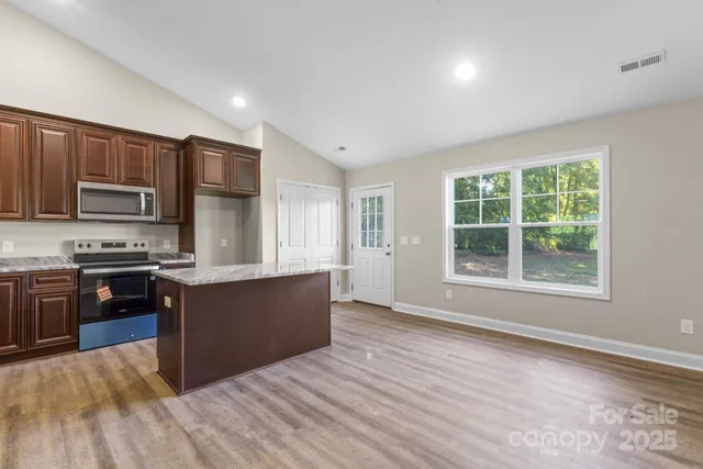 a large kitchen with stainless steel appliances granite countertop a stove a sink dishwasher a microwave oven and a refrigerator with wooden floor