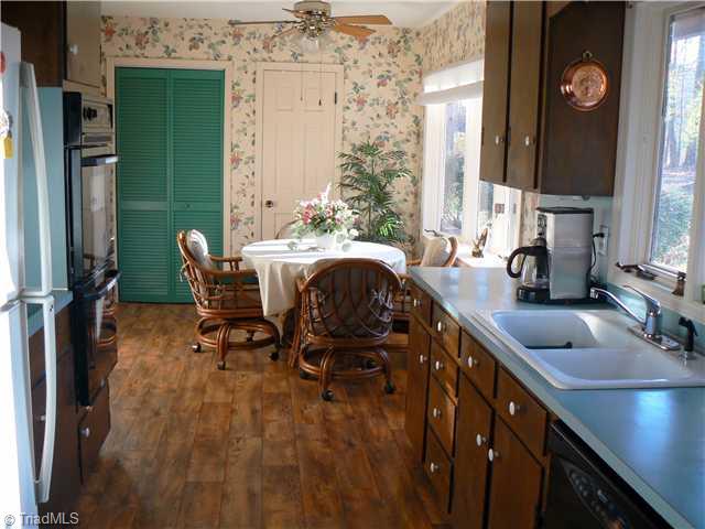 2444 Scott Mountain Road Asheboro, NC 27205 - Photo 5 of 16 Kitchen. The green folding door opens to a pantry. The white door leads to the laundry. The kitchen has double ovens, a stove top and dishwasher. Floor appears to be wood but is actually vinyl. Note the bow window near the dining area overlooking backyard.