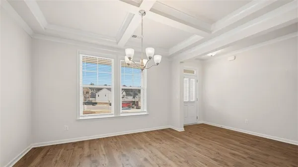 an empty room with wooden floor chandelier and windows