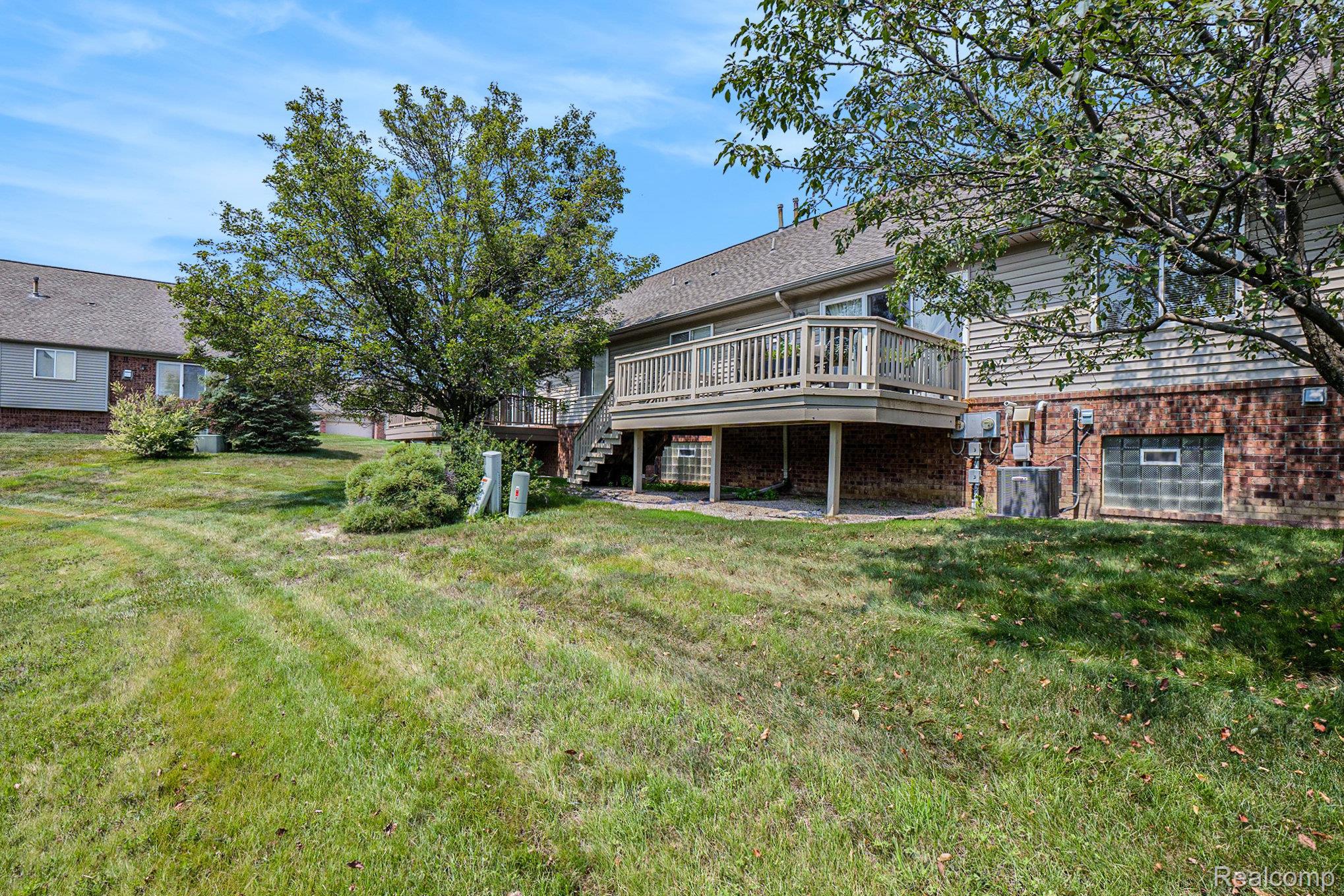 5477 Victory Circle Sterling Heights, MI 48310 - Photo 32 of 32 Rear exterior featuring a wood-decked balcony with staircase access to the lawn, brick lower-level facade, and mature trees providing natural shading