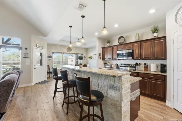 a kitchen with stainless steel appliances granite countertop a stove a refrigerator a kitchen island a dining table and chairs with wooden floor