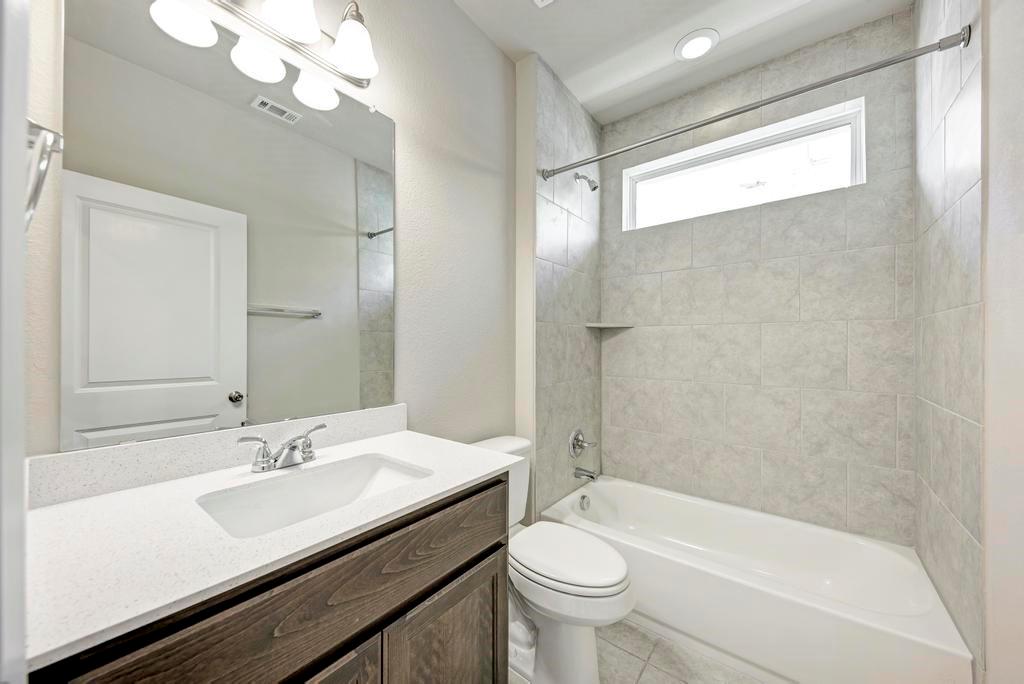 1209 Goforth Road Kyle, TX 78640 - Photo 24 of 32 A well-lit primary bathroom features a pristine vanity and a tiled shower-tub combination.