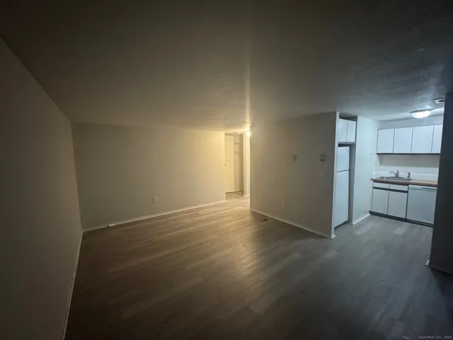 a view of empty room with wooden floor and kitchen