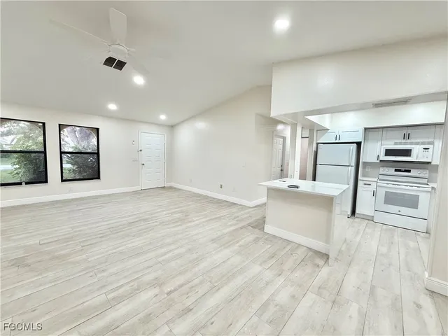 a large white kitchen with kitchen island a stove a sink dishwasher and a refrigerator with wooden floor