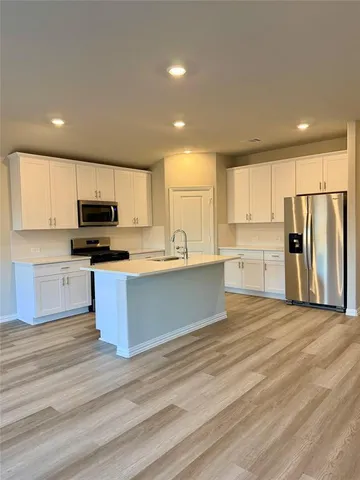 a large kitchen with stainless steel appliances granite countertop a stove a refrigerator a sink a microwave and white cabinets with wooden floor