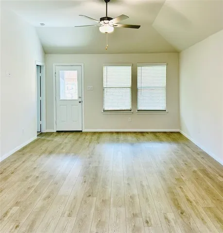 an empty room with wooden floor chandelier fan and windows