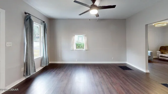 an empty room with wooden floor fan and windows