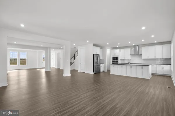 a view of an empty room with wooden floor and a kitchen