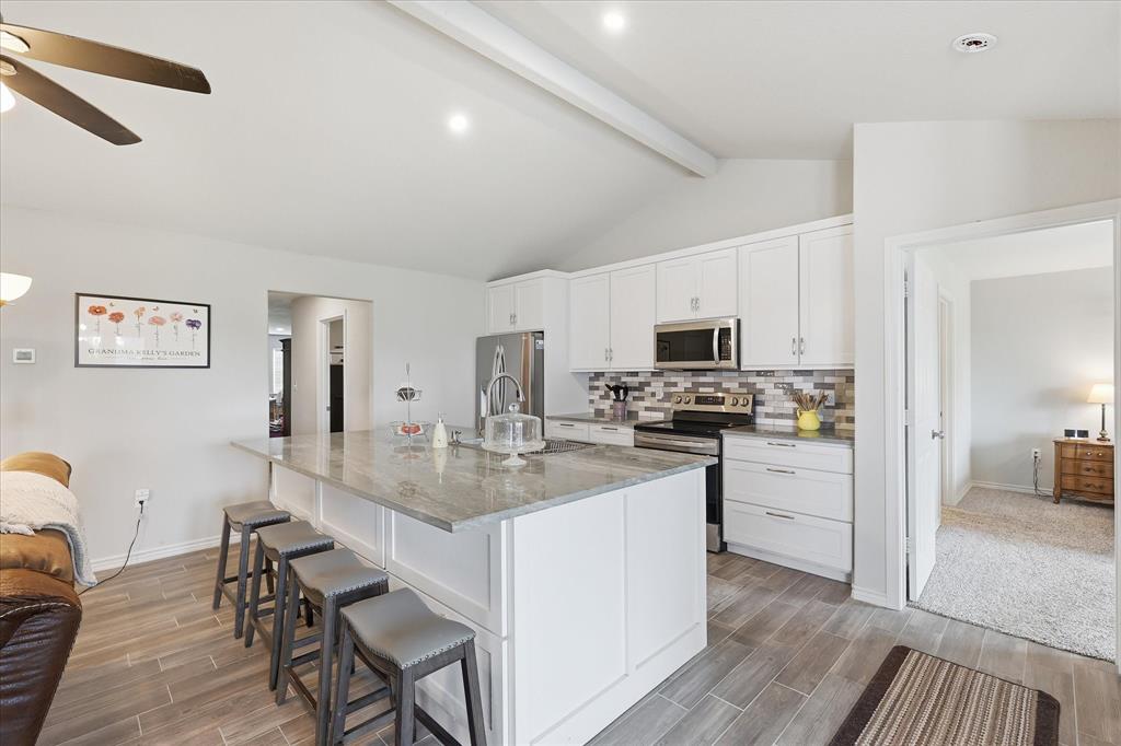 110 Highview Road Ennis, TX 75119 - Photo 12 of 40 Kitchen featuring white cabinetry, stainless steel appliances, a multi-tone tile backsplash, a large island with a light-toned countertop, and wood-finish flooring
