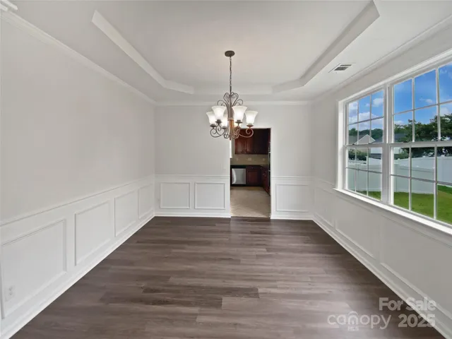 a view of a room with wooden floor chandeliers and kitchen view