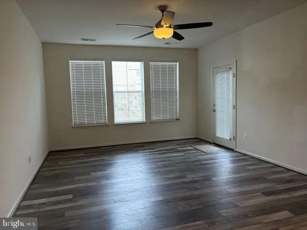 an empty room with wooden floor chandelier fan and windows