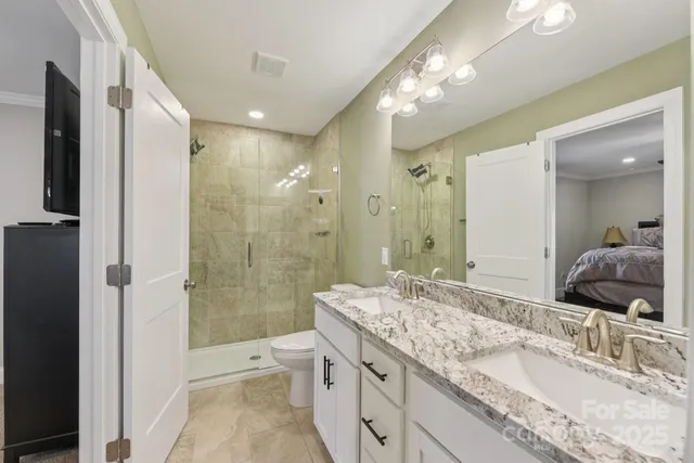 a bathroom with a granite countertop double vanity sink toilet mirror and shower
