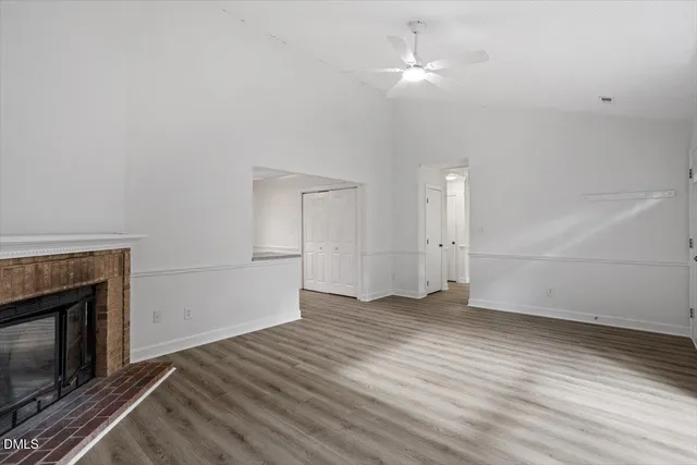 an empty room with wooden floor a ceiling fan a fireplace and windows