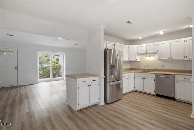 a kitchen with granite countertop a refrigerator a sink dishwasher a stove and white cabinets with wooden floor