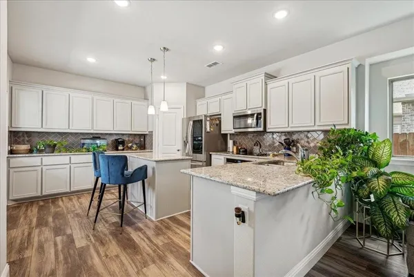 a kitchen with kitchen island granite countertop a stove a sink a microwave and white cabinets with wooden floor