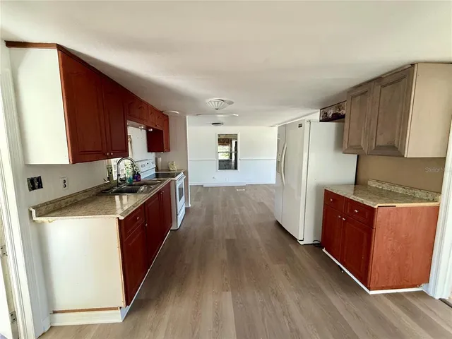 a kitchen with granite countertop wooden floors wooden cabinets a sink and appliances