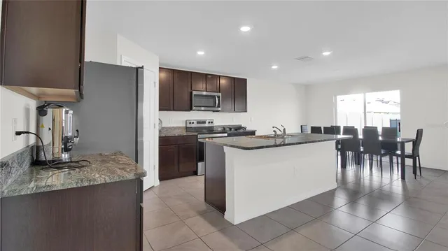 a kitchen with stainless steel appliances granite countertop a table chairs sink and cabinets