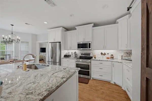 a kitchen with stainless steel appliances granite countertop a stove top oven a sink a refrigerator and white cabinets