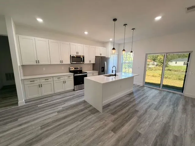 a large white kitchen with kitchen island a stove a refrigerator a sink dishwasher and white cabinets with wooden floor