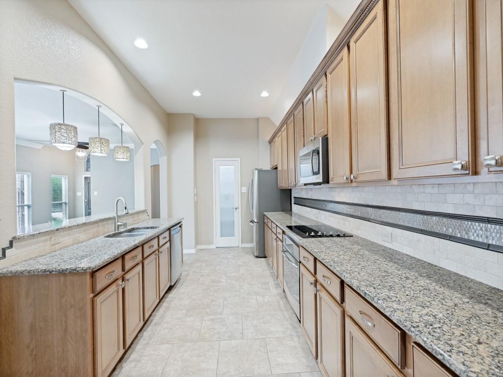 10032 Bell Rock Road Frisco, TX 75035 - Photo 11 of 23 Galley kitchen featuring extensive wood cabinetry, speckled stone countertops, stainless steel appliances, a tile backsplash with decorative accent, and recessed lighting.